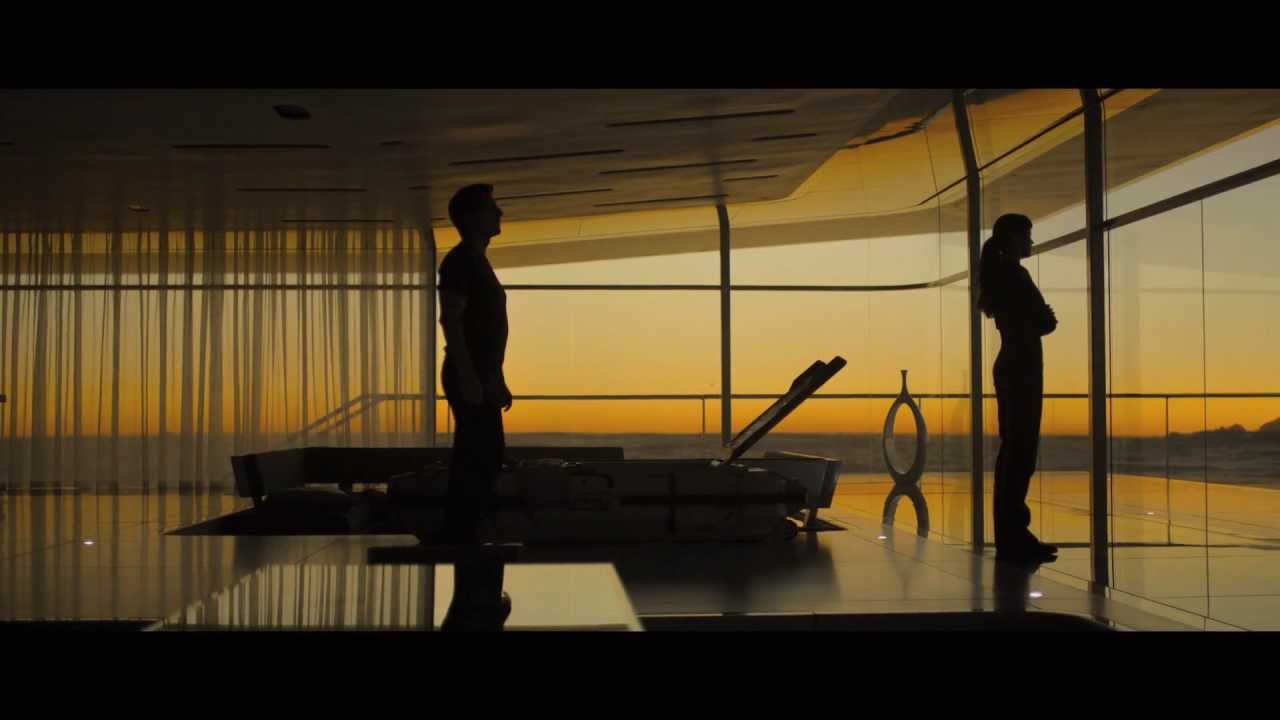 A glass-walled penthouse interior at sunset — two figures silhouetted against a golden horizon, the room flooded with warm directional sunlight